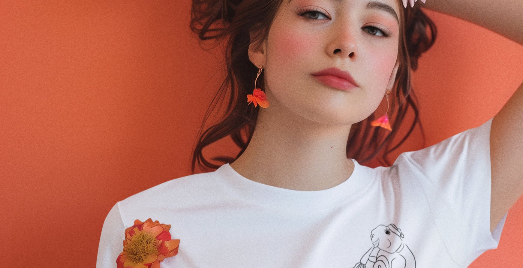 Woman wearing a floral headpiece and white t-shirt with floral designs against an orange background